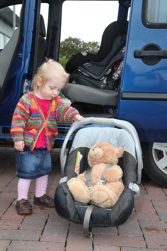 Photo of a toddler with their teddy tucked safely into a car seat